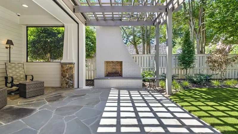 A flagstone patio with a stone fireplace and a timber pergola overhead